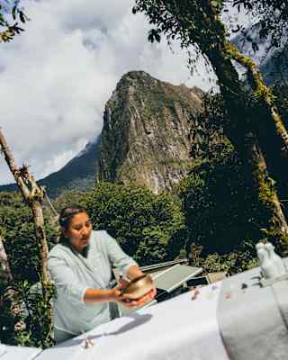 Angled image of a spa therapist as she prepares an outside table with bells and bowls, against a Huayna Picchu backdrop.