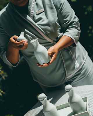 Angled image of spa staff in grey uniform, from the neck down, holding a bottle and lid at a table with two more containers.