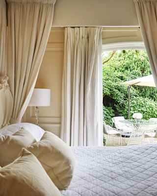 Pillowy four-poster bed with a view through patio doors to a garden area beyond