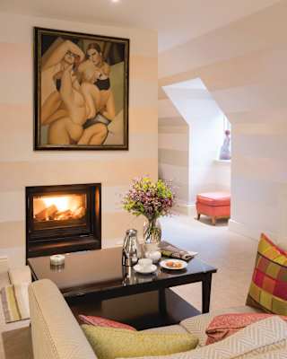 A modernist painting of nudes hangs above a wood burning stove. Pale pink and white horizontal stripes cover every wall