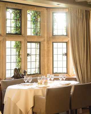 A table set for four occupies the bay of a stone mullioned window nook. A small bronze figure sits on the window sill