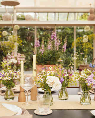 The Victorian glasshouse is set for a summer lunch, with vases full of Marguerites and Sweet Peas, candles and glassware