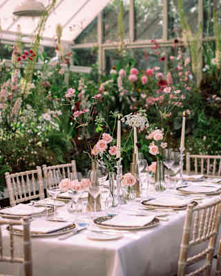 A laid table with pink roses and candles waits for guests in the magical Hartley botanic glasshouse, filled with hollyhocks.