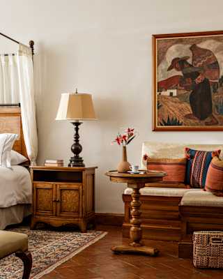 In a suite detail, a padded corner bench with woven cushions provides a lounge area, with a round table and large wall art above.