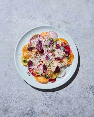 Looking down on a vibrant salad of finely sliced radish and beets, scattered with grated cheese, leaves and grains.