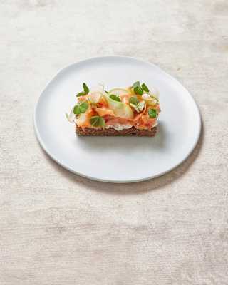 A traditional chapla bread with trout, shaved olluco and citrus, served on a simple white plate on a pale-painted table.
