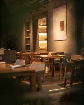 Eye-level view through an empty restaurant dining room, with wood and natural hues, and with warm spot-lit areas.
