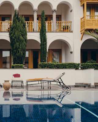 In front of the hotel, a table, two pots and three metal loungers sit at angles by the pool, reflected in its mirror surface.