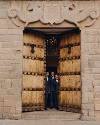 Three suited staff members open the grand principal doors of Palacio Nazarenas with big smiles.