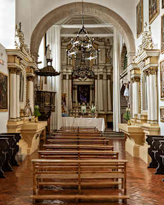 Old pews and eighteenth-century gold-framed artworks line the chapel walls either side of bench-seating facing the altar.
