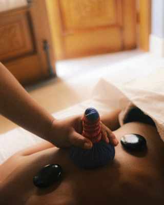Close-up of a therapist's hand as she applies a compress to the back of a guest receiving a treatment with massage stones.