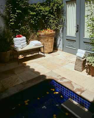 A bench stacked with white towels sits in sun outside the door of Hypnôze Spa in a courtyard with a plunge pool and plants.