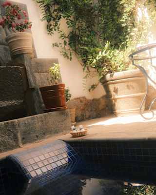 Two compresses sit on a basket on the ground of a courtyard with cool shade and plants, seen at eye-level from a plunge pool.