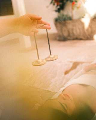 View of a hand holding a string with a cymbal at either end above the face of a woman indulging in a therapy at Hypnôze Spa.