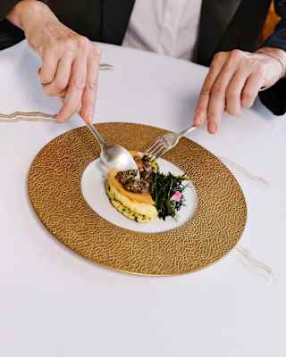 A diner cuts into a smoked duck egg with peverada, morels and Monte Veronese cheese, served on a gold-edged plate.