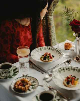 Two guests gaze through the window at an Afternoon Tea in the Cygnus Car with fruit tartlets, pastries, cocktails and coffee.