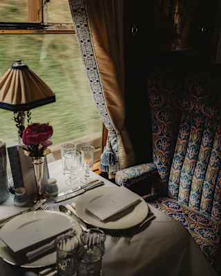 Looking down on a dining table in the Audrey Car with glasses, plates and cutlery for two, part shaded by a sweep of curtain.