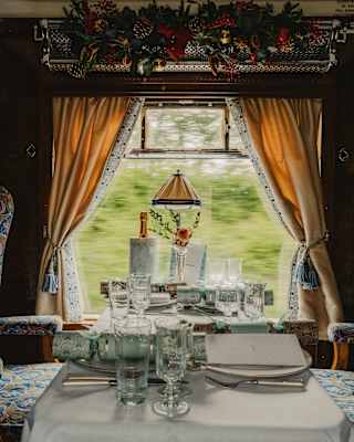 In a face-on view of an Audrey Car table, water and wine glasses gleam at a setting for two, flanked by wide plush chairs.