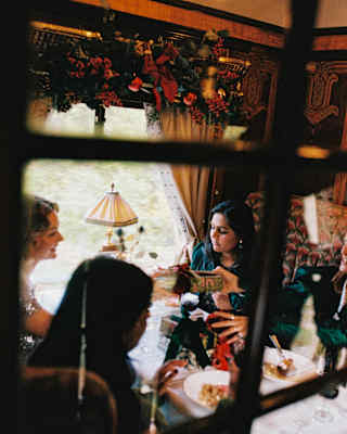 View through a glass-panelled door of a carriage filled with festive decorations and four happy diners with plates of food.