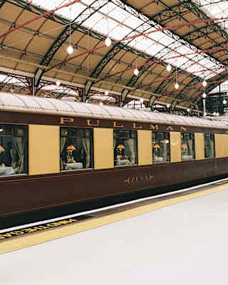 View of the Zena carriage's yellow and mauve exterior as it waits under the iconic roof of London's Victoria Train Station.