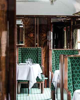 French polished wood panelling on walls and chair frames catches the light. Gilt framed mirrors feature zigzag art deco edges