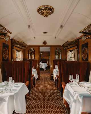 View down the Phoenix carriage aisle with geometric-pattern carpet in browns, flanked by white dining tables and russet chairs.