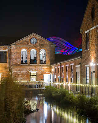 Night view of Laverstoke Mill, now the Bombay Sapphire Distillery, with its walkway fairy lights reflecting in the River Test.