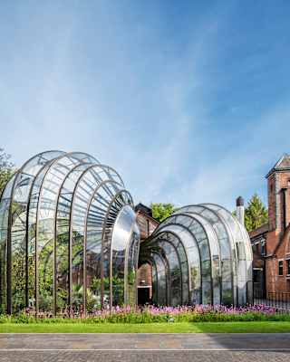 Two intertwined botanical glasshouses with a bulbous funnel design, set on lawned gardens between red-brick buildings.