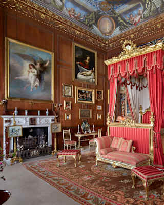 A Tudor Burleigh House bedroom revels in opulence with a vivid red four-poster bed with gilt touches, chaise-longue and art.
