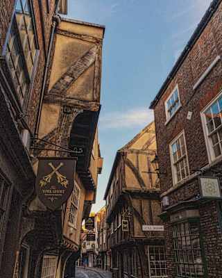 View of The Shambles in York where ancient beamed buildings lean, heads almost together, over a medieval cobbled lane.