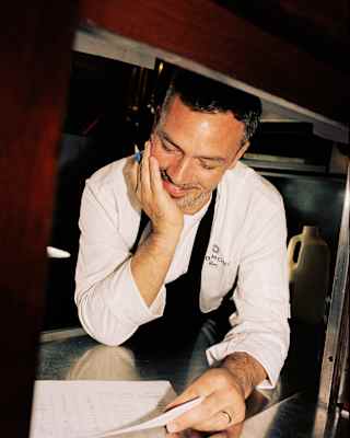 Head Chef Jon Freeman, in whites and a black apron, rests his hand on his chin as he leans on the pass, looking at paperwork.