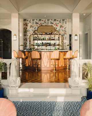 On 1891 Bar's raised parquet floor, six striped stools line a curved counter in front of an Art Deco mirrored bottle shelf.