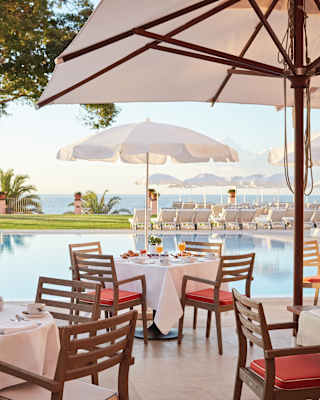 Linen-topped tables under sun umbrellas on a poolside restaurant terrace