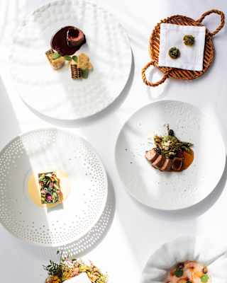 A selection of Chef Costa's amuse-bouches and signature dishes served on four white plates, a floral bed and a wicker basket.