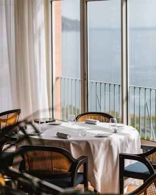 A window table with a white tablecloth, water glasses and napkins, and four cane chairs, claims a spectacular sea view.