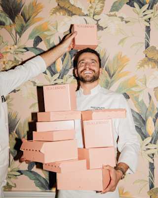 Pastry Chef, António Morgado laughs as he stands, arms full of pink cake boxes, while a chef balances another on his head.