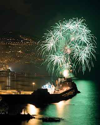 White and green star-cluster fireworks light up the night sky above Funchal marina, casting a peppermint hue on the water.