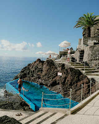 Below the sea platform where loungers and parasols catch sun and spray, two men enjoy the rock pool's proximity to the ocean.