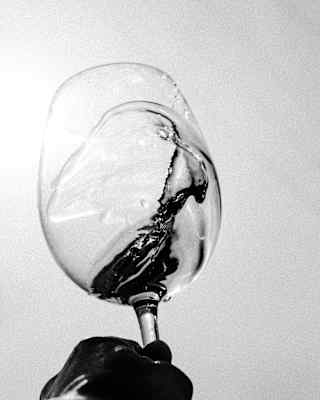 Black and white low-angle image of wine lapping the inside of a wineglass, as it is swirled by a hand holding the stem.