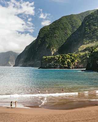 Lush coastal mountains dive into the blue waters at Seixal Beach, where the black sand looks momentarily golden in the sun.