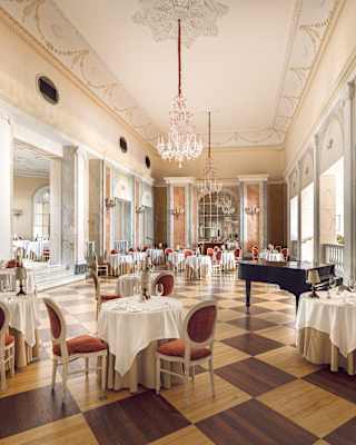 Tables await guests in the vast mirrored dining room, which has a grand piano, chandeliers and a stunning chessboard floor.