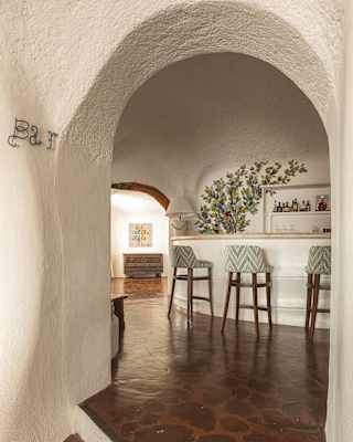 View through a white-rendered internal doorway into an area where three grey, high-back stools line a curved white bar.