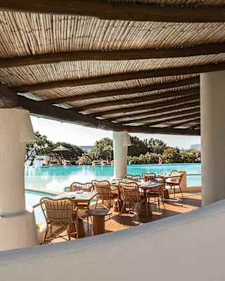 Bordering the still, sapphire, split-level pools, the Pool Bar's tables and chairs rest beneath a fanned rattan terrace shade.