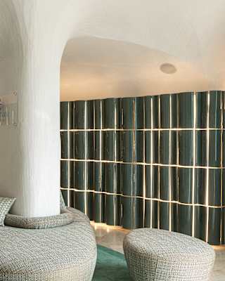 Upholstered benches wrap around wall supports in the reception area, where backlit green wall tiles create an intimate glow.