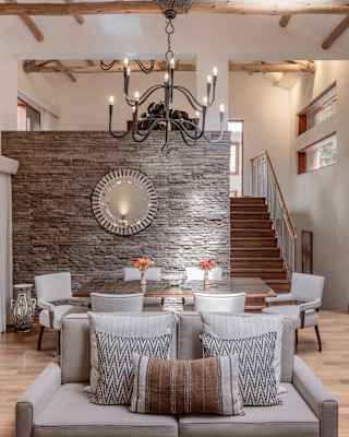 View over a beige sofa to a dining table and behind, a stone partition wall with a staircase, right, up to the next level.