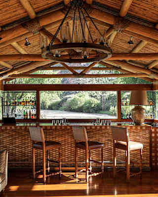 Beneath a wood-beamed roof, three high-back stools sit along the bar at El Huerto Bar with a direct view to the Urubamba River.