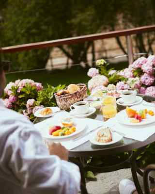 Angled image of a breakfast table, with plates of diced fresh fruit, a basket of bread, two cups of coffee and juice.