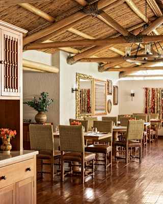 View across El Huerto's interior, capturing dining tables and chairs with olive backs and wooden criss-cross ceiling beams.
