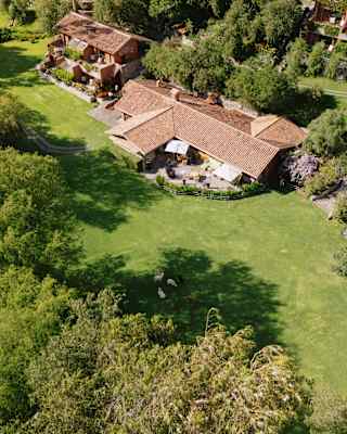 Aerial view of Rio Sagrado's main building and separate rooms with flowering balconies, set in lush lawns, circled by forest.