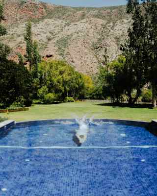 There's a splash as a guest dives into the blue-tiled pool in the hotel gardens, with a backdrop of rugged mountains.